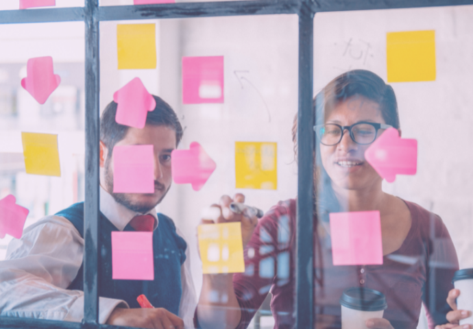 Two team members brainstorm using colorful post-its on office window