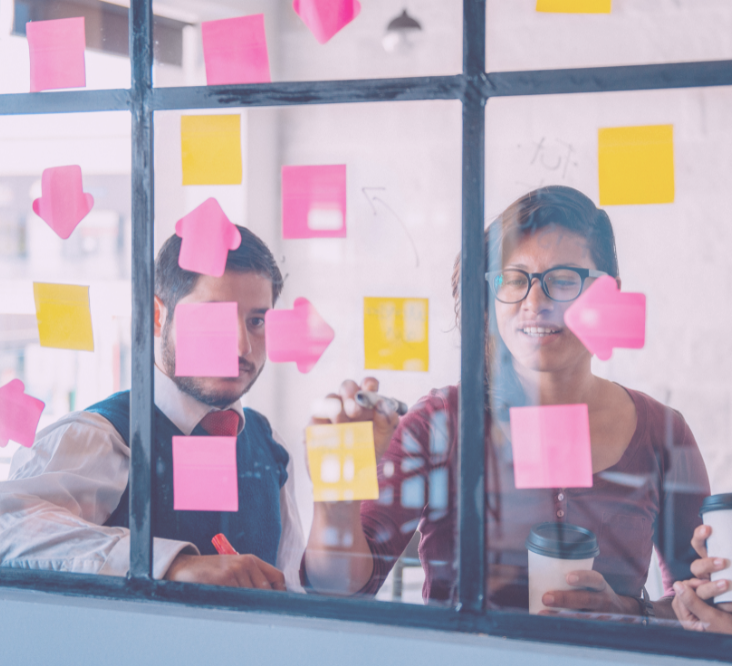 Two team members brainstorm using colorful post-its on office window